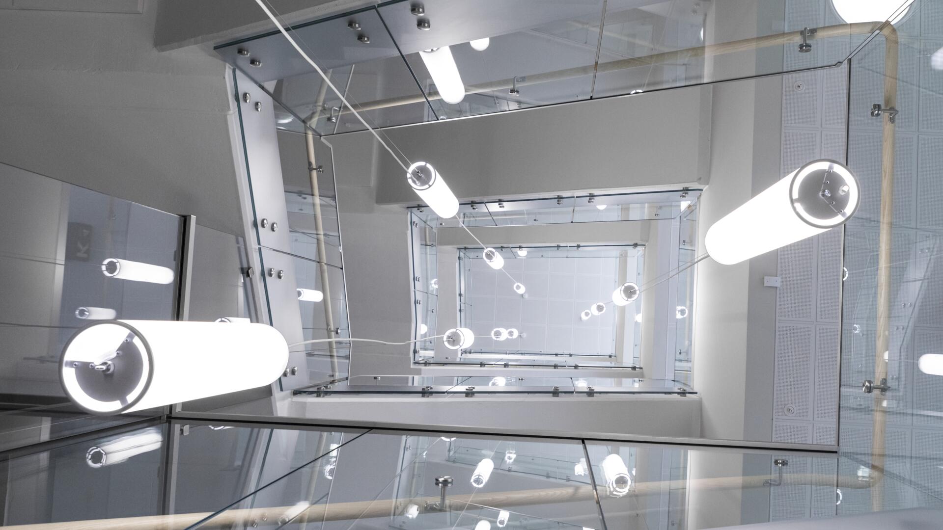 Ett trapphus i glas sett underifrån med ljuskäglor hängandes i en formation som skapar en vacker abstrakt form.